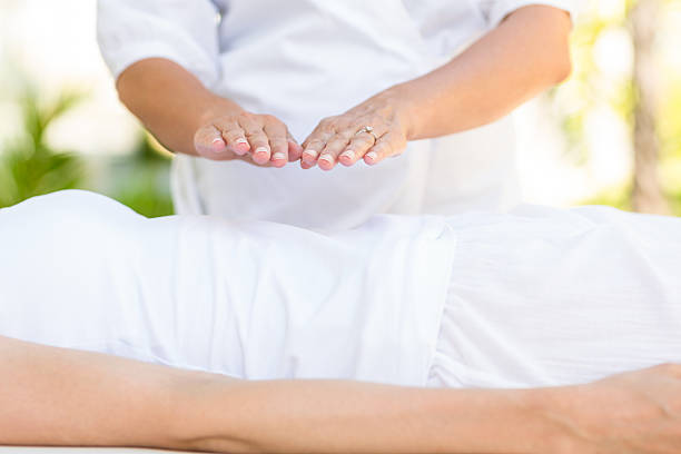 Femme calme, vêtue de blanc, recevant un traitement reiki dans une ambiance lumineuse et sereine